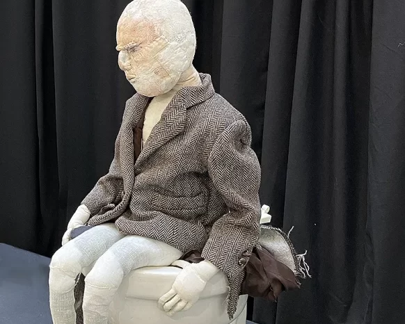 Boy with tweed jacket sitting on a cubicle with overflowing fabrics.