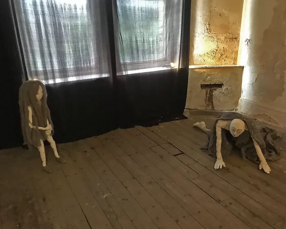 Two female sculptures 3 metres apart. A girl standing up with long woolly hair, the other a woman who crawls on the floor with a woollen blanket over her back