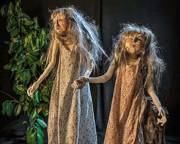 Two girl sculptures walking through a dark garden