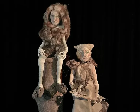 Two male sculptures in prehistoric clothes in front of dark background.