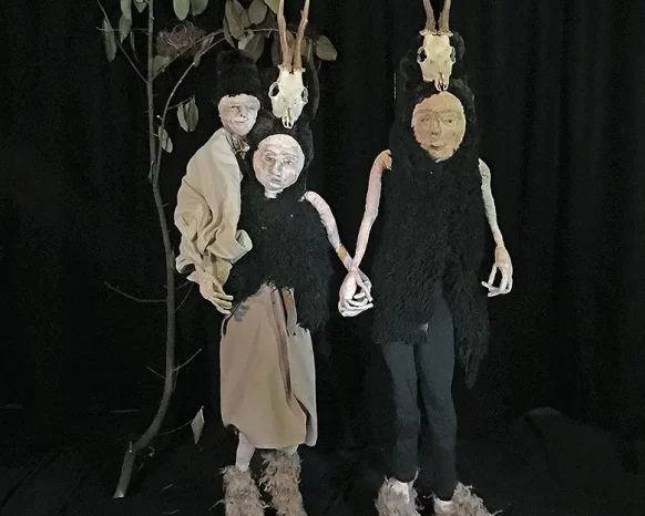 Male and female sculptures with a child in prehistoric clothes in front of dark leafy background