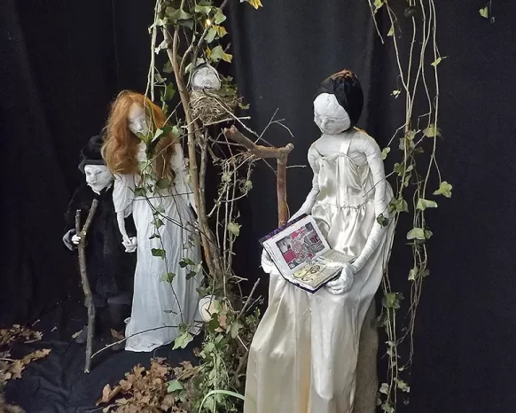 Staging of two girl sculptures and one boy within branches and leafs