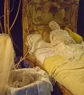 Human sculpture of woman in yellow bed with cradle in foreground