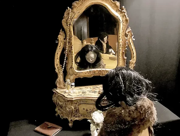 Woman figure sitting at antique dressing table looking into mirror.